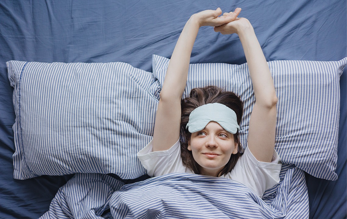 Eine Frau die sich im Bett streckt und eine Schlafmaske an hat