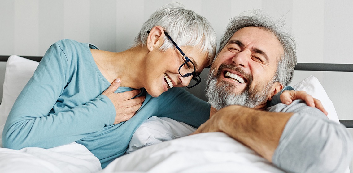 Ein Paar, das glücklich nebeneinander im Bett liegt und lachen