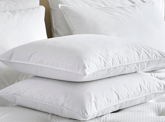 Zwei weiße Kopfkissen auf einem Bett, aufeinander liegend